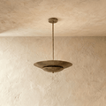 Clérachic pendant light in vintage brass, its wide disc shade suspended from a slender rod against plaster.