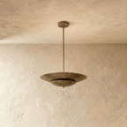 Clérachic pendant light in vintage brass, its wide disc shade suspended from a slender rod against plaster.
