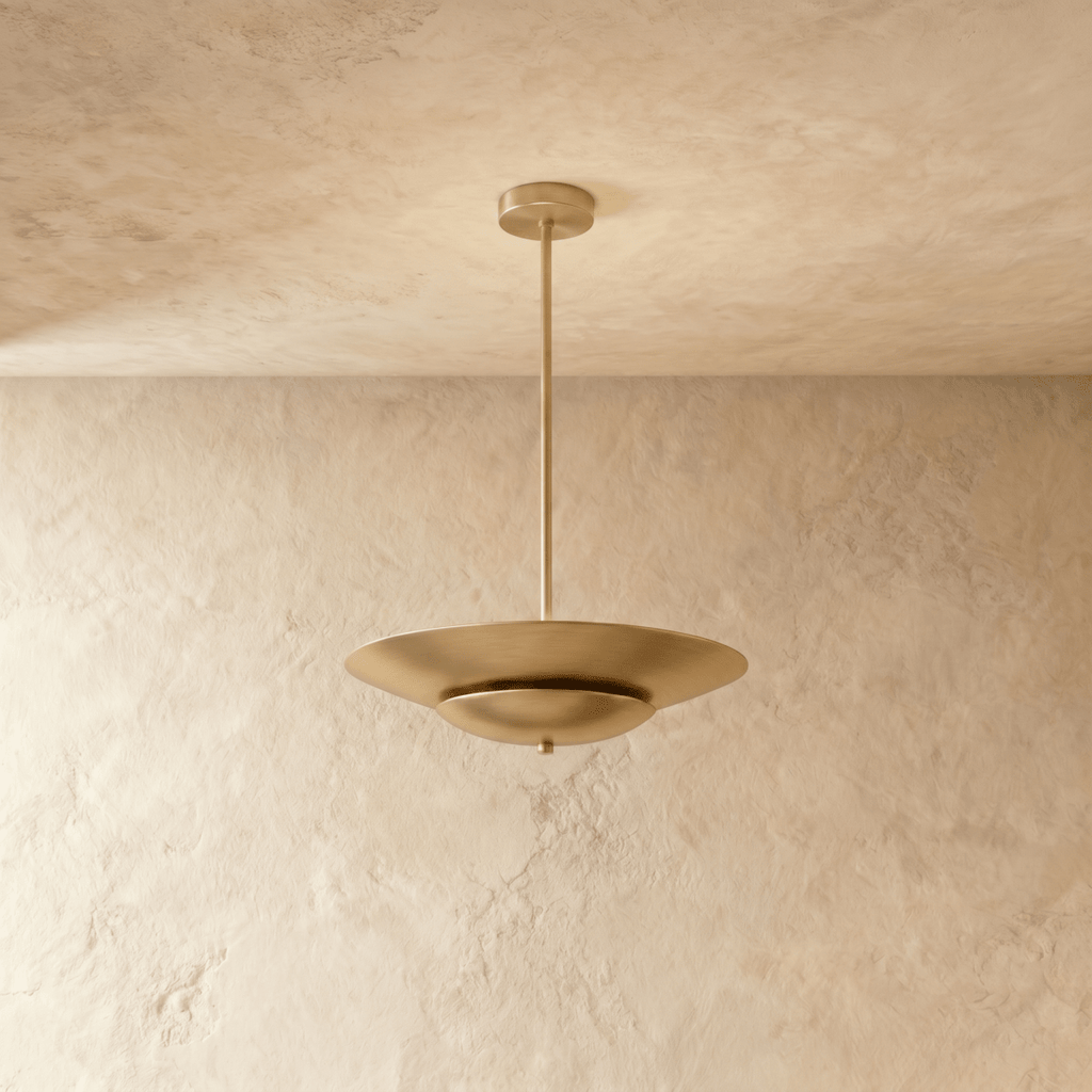 Clérachic pendant light in brushed brass, a wide saucer shade hanging from a slim rod near a plaster wall.