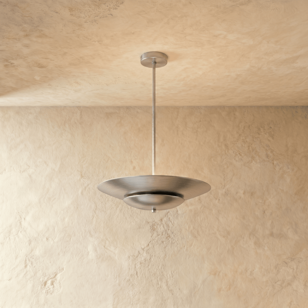 Clérachic pendant light in brushed chrome, its wide disc shade suspended from a slender rod against plaster.