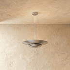 Clérachic pendant light in brushed chrome, its wide disc shade suspended from a slender rod against plaster.