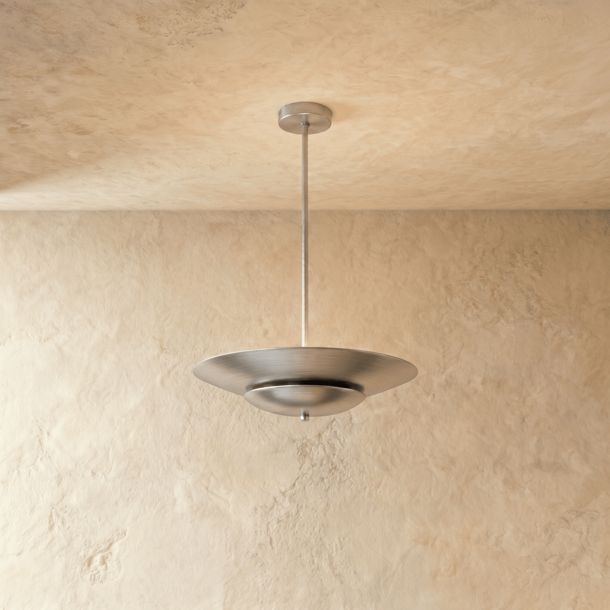 Clérachic pendant light in brushed chrome, its wide disc shade suspended from a slender rod against plaster.