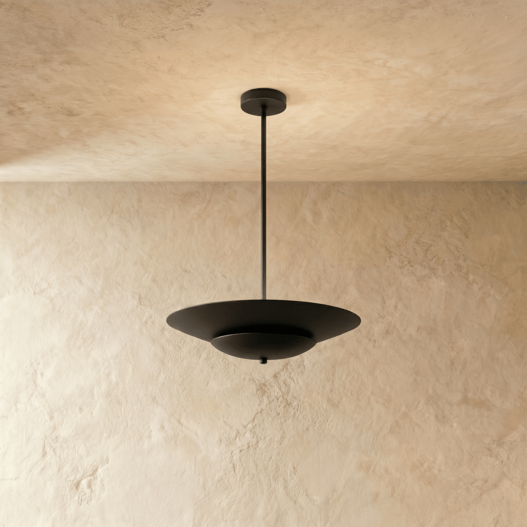 Clérachic pendant light in matte black, a wide disc shade hanging from a slim rod against a plaster wall.