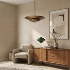 Clérachic pendant light in vintage brass lighting a living room corner beside a wood credenza and armchair.