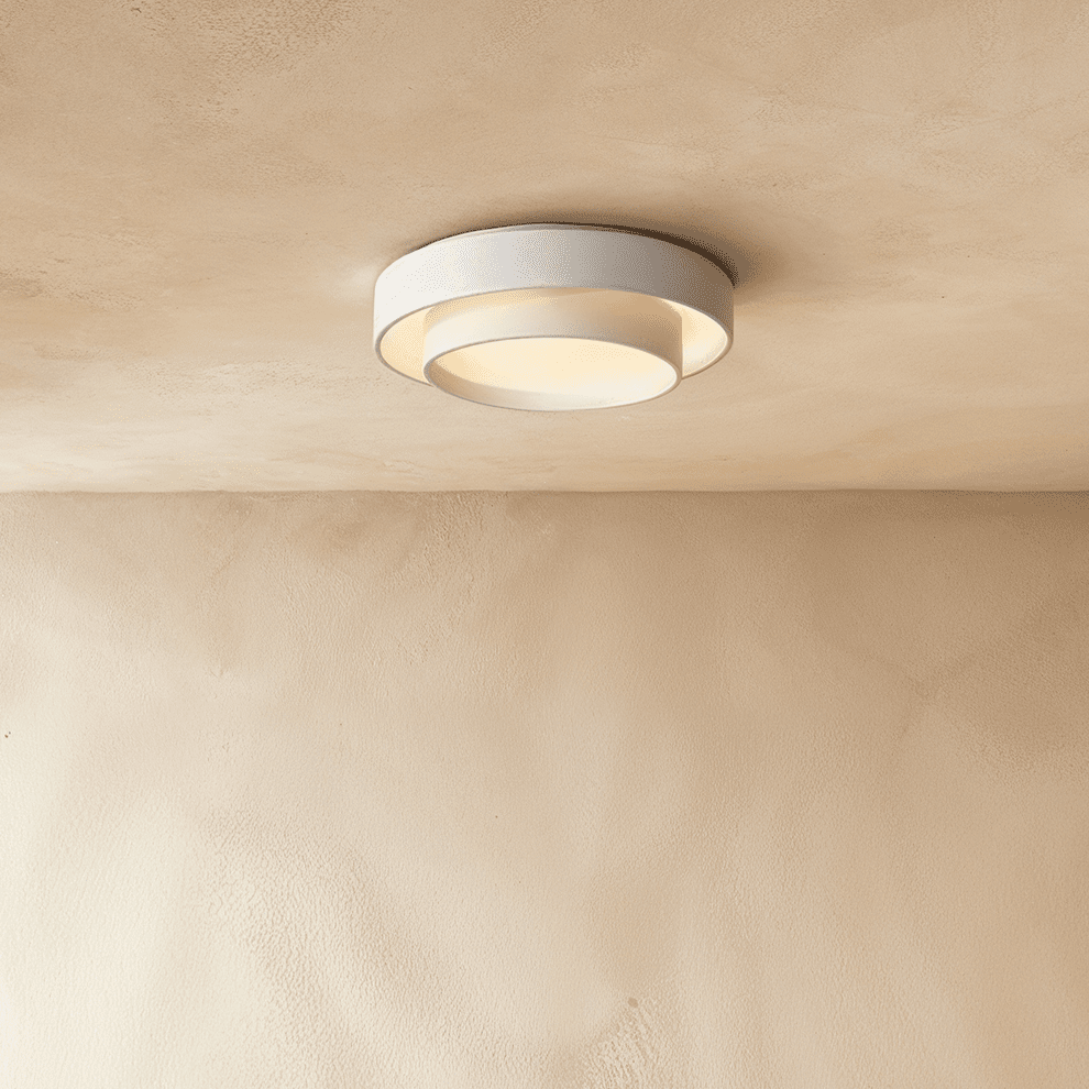 Clérachic white layered round flush ceiling light seen from below, its inner drum lit warmly against a plastered ceiling.