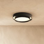 Clérachic black two-tier round ceiling light with an inner drum offset inside a wider ring, lit softly on a limewash ceiling.