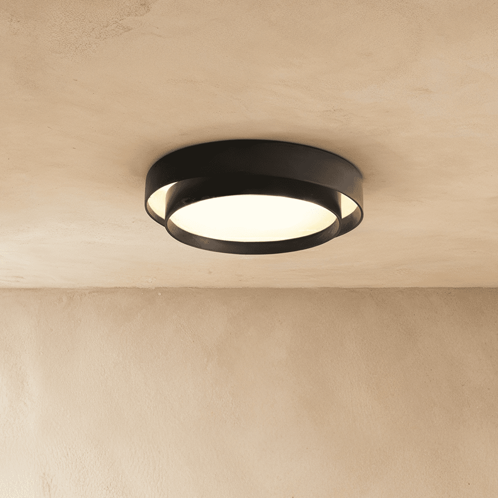Clérachic black two-tier round ceiling light with an inner drum offset inside a wider ring, lit softly on a limewash ceiling.