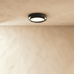 Clérachic black layered round ceiling light set high on a plastered ceiling above a pale limewash wall.