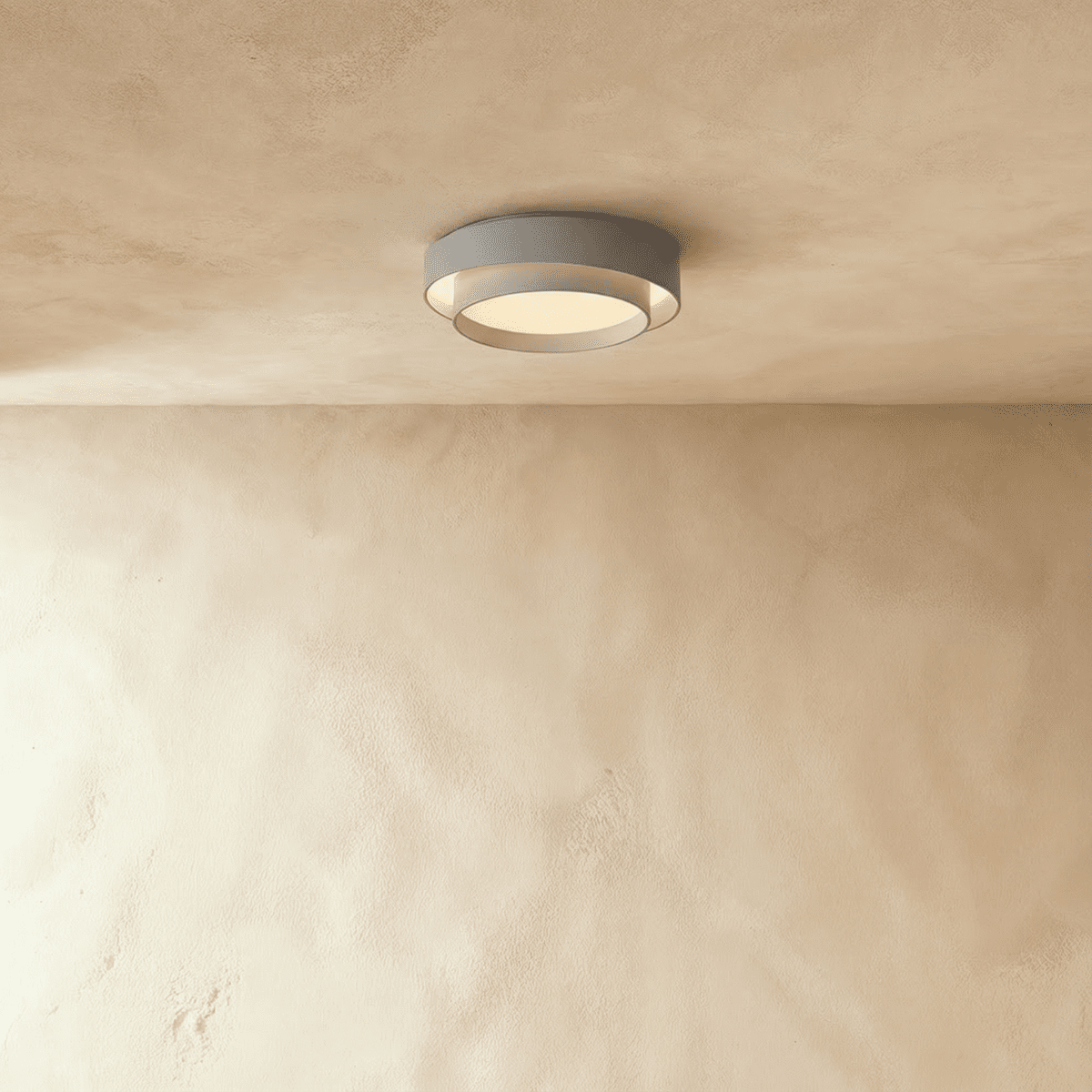 Clérachic grey layered ceiling light with a pale inner drum and soft glow, mounted above a limewash wall.