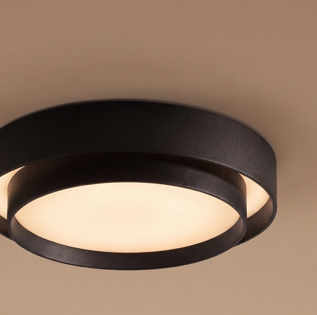 Close view of a Clérachic black layered ceiling light, its leather-textured outer ring framing a glowing frosted centre.