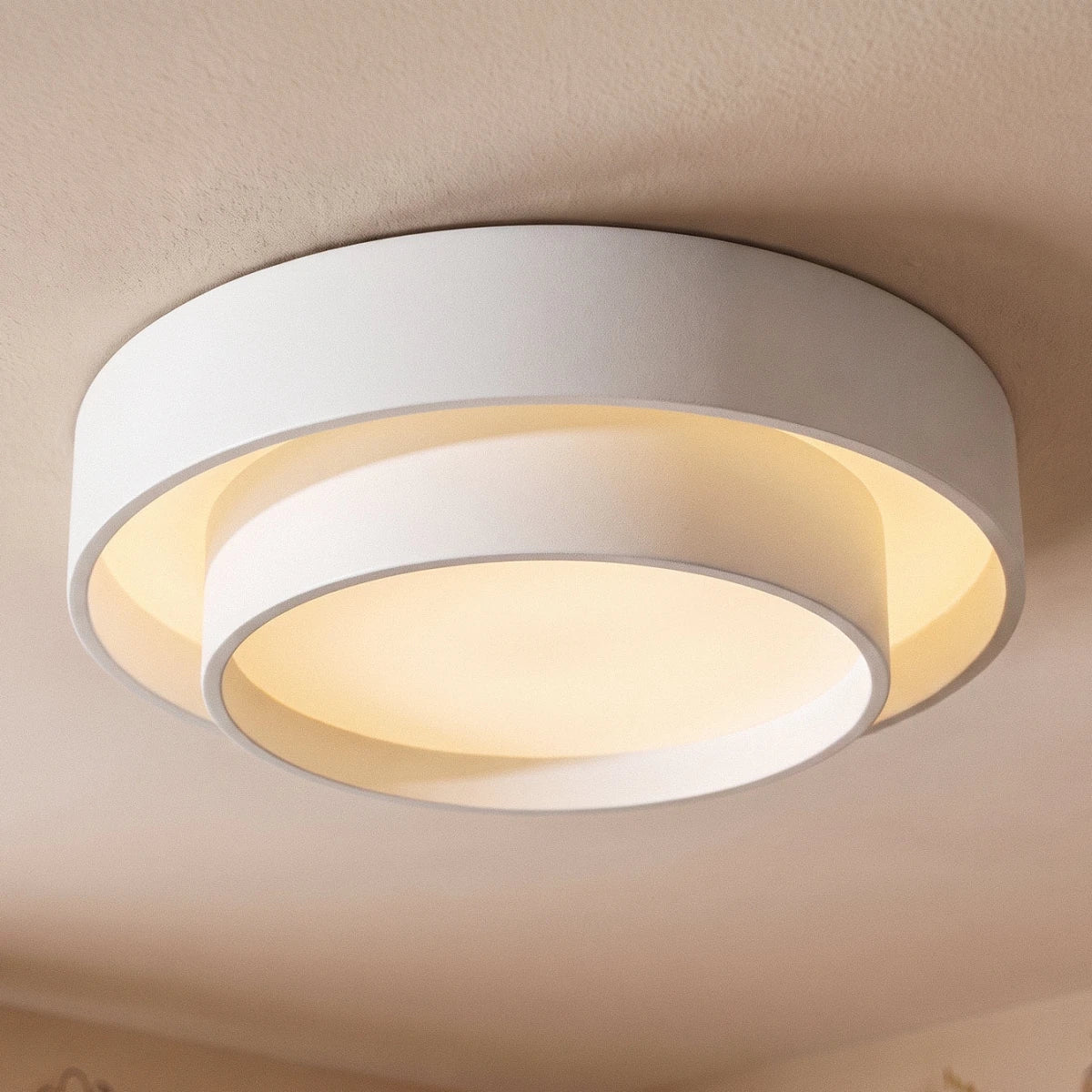Close view of a Clérachic white layered ceiling light, the offset inner drum and outer ring lit with a warm glow.