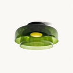 A green layered glass Clérachic ceiling light, lit, with a black canopy and a glowing disc, on a plain white backdrop.