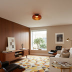 An orange glass Clérachic ceiling light over a living room with a walnut wall, a sideboard and a geometric rug.