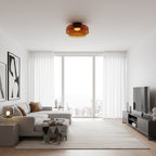 An orange glass Clérachic ceiling light in a bright living room with floor-to-ceiling windows and sheer curtains.