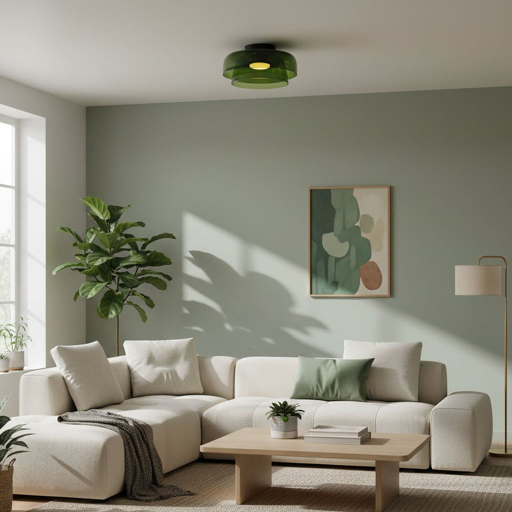 A green glass Clérachic ceiling light over a cream sofa and a fiddle-leaf plant, against a sage-green wall.