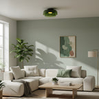 A green glass Clérachic ceiling light over a cream sofa and a fiddle-leaf plant, against a sage-green wall.
