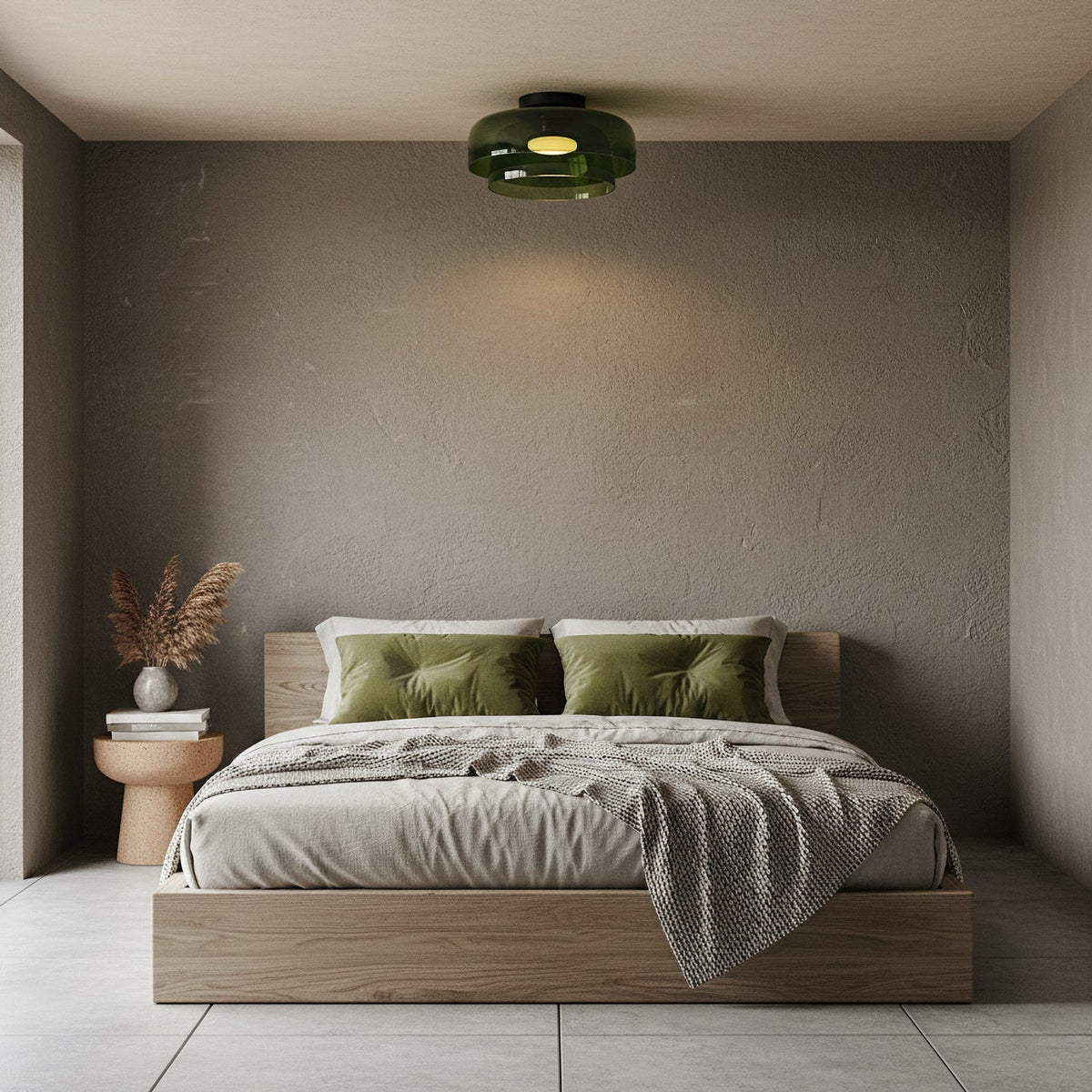 A green glass Clérachic ceiling light above a low platform bed with olive cushions, against a textured taupe wall.
