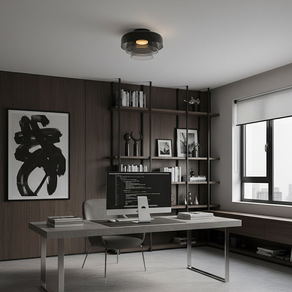 A smoky grey glass Clérachic ceiling light over a home office desk, with dark wood panelling and open shelves behind.