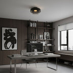 A smoky grey glass Clérachic ceiling light over a home office desk, with dark wood panelling and open shelves behind.