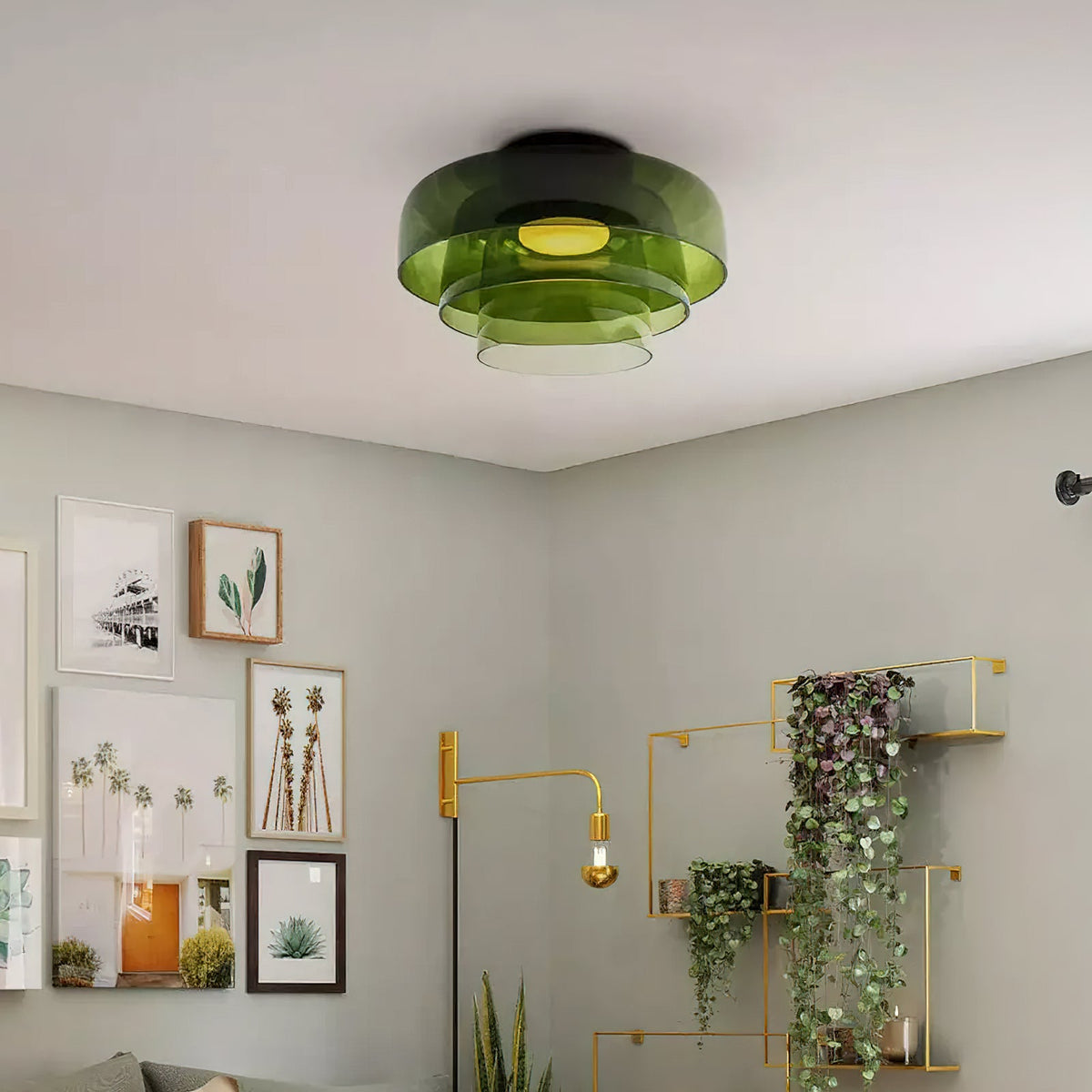 A green layered glass Clérachic ceiling light in a grey room with framed prints and a gold wall shelf of trailing plants.
