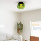 A green layered glass Clérachic ceiling light in a white room with dried palm leaves and a cream sofa below.