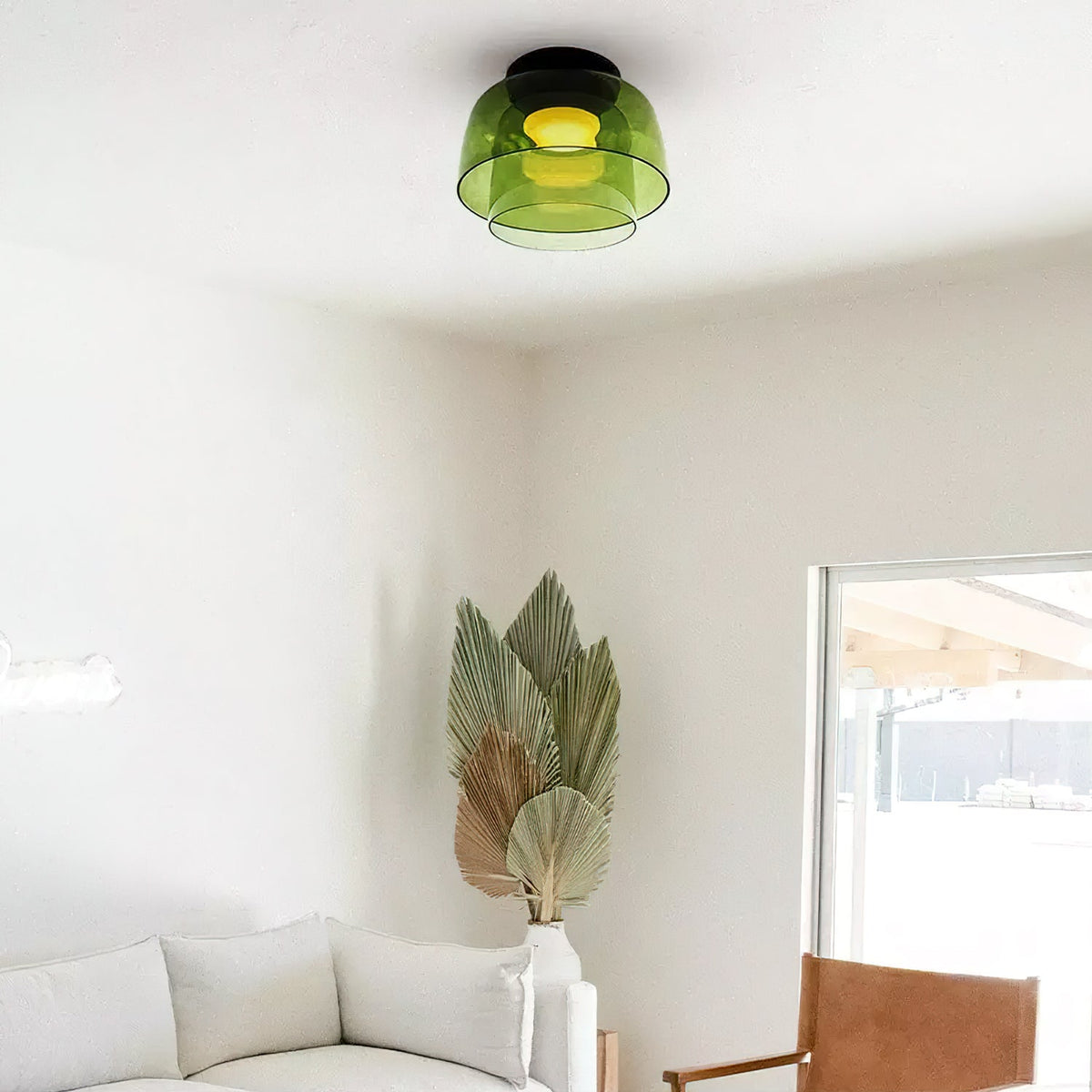 A green layered glass Clérachic ceiling light in a white room with dried palm leaves and a cream sofa below.