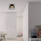 A smoky grey glass Clérachic ceiling light in a white open-plan space with a dining table in the distance.