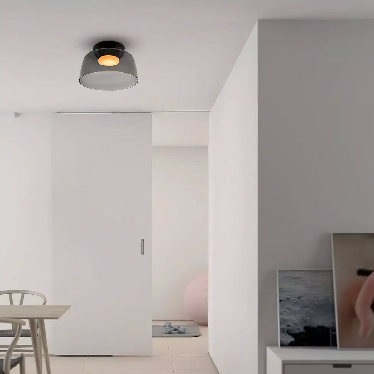 A smoky grey glass Clérachic ceiling light in a white open-plan space with a dining table in the distance.