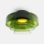 A green glass Clérachic ceiling light with three stepped layers, lit, on a pale grey backdrop.