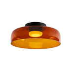 A wide, shallow orange glass Clérachic ceiling light with a black canopy and a glowing disc, on a white backdrop.