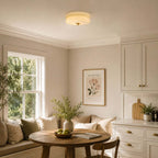 This Clérachic flush mount ceiling light glows over a breakfast nook with a window seat, a round table and a framed floral print.