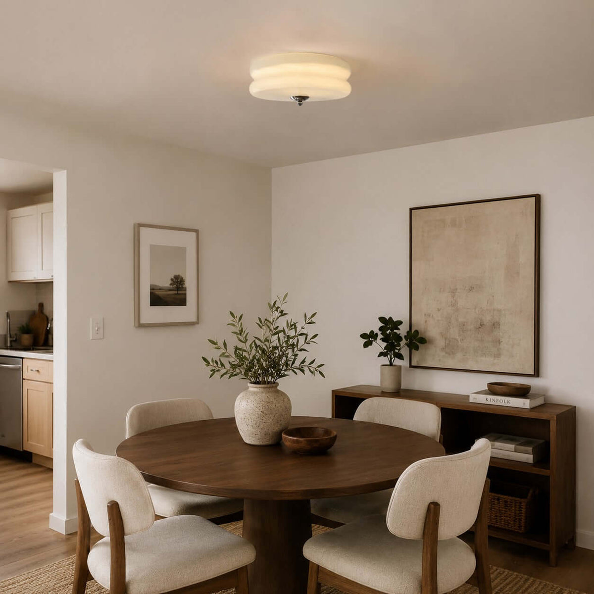 A Clérachic ceiling light with a layered glass shade hangs low above a round walnut dining table and cream wooden chairs.