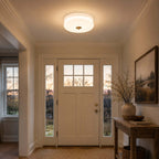 Warm light from a Clérachic flush mount falls in an entrance hall with a glazed front door, side windows and a wooden console.