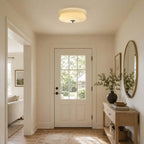 A Clérachic ceiling light with a stepped glass shade lights a small entryway with a glazed door, an oval mirror and a console.