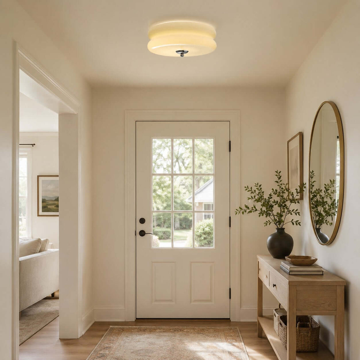 A Clérachic ceiling light with a stepped glass shade lights a small entryway with a glazed door, an oval mirror and a console.