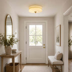 Clérachic flush mount lit above a hallway with a white glazed door, an arched mirror, a console table and a bench with a basket.