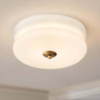 Close view of the stepped white glass shade and brass-toned finial of this Clérachic flush mount, seen from below.