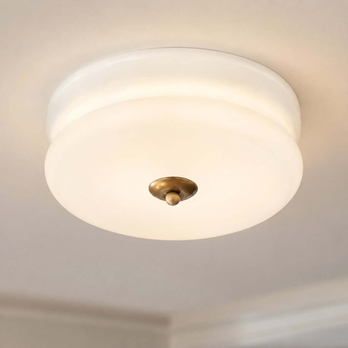 Close view of the stepped white glass shade and brass-toned finial of this Clérachic flush mount, seen from below.