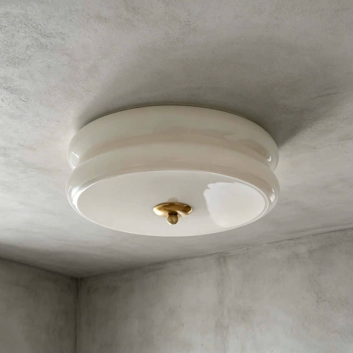 A beige and gold Clérachic flush mount with a layered glass shade and a brass-toned finial, seen against a grey limewash ceiling.