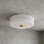 A white and gold Clérachic flush mount with a layered milky glass shade and a gold finial, seen on a grey limewash ceiling.