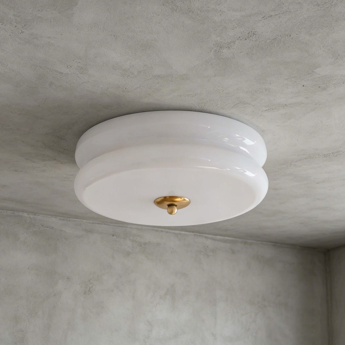 A white and gold Clérachic flush mount with a layered milky glass shade and a gold finial, seen on a grey limewash ceiling.