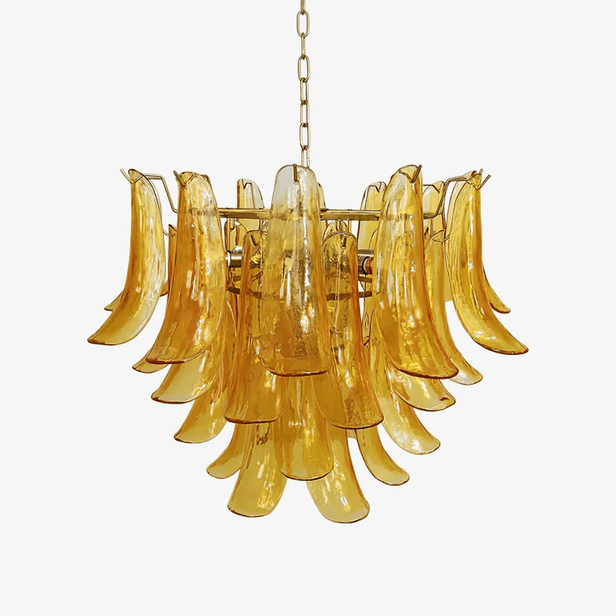 Layered amber glass leaf chandelier from Clérachic with a gold frame and hanging chain, on a plain pale backdrop.