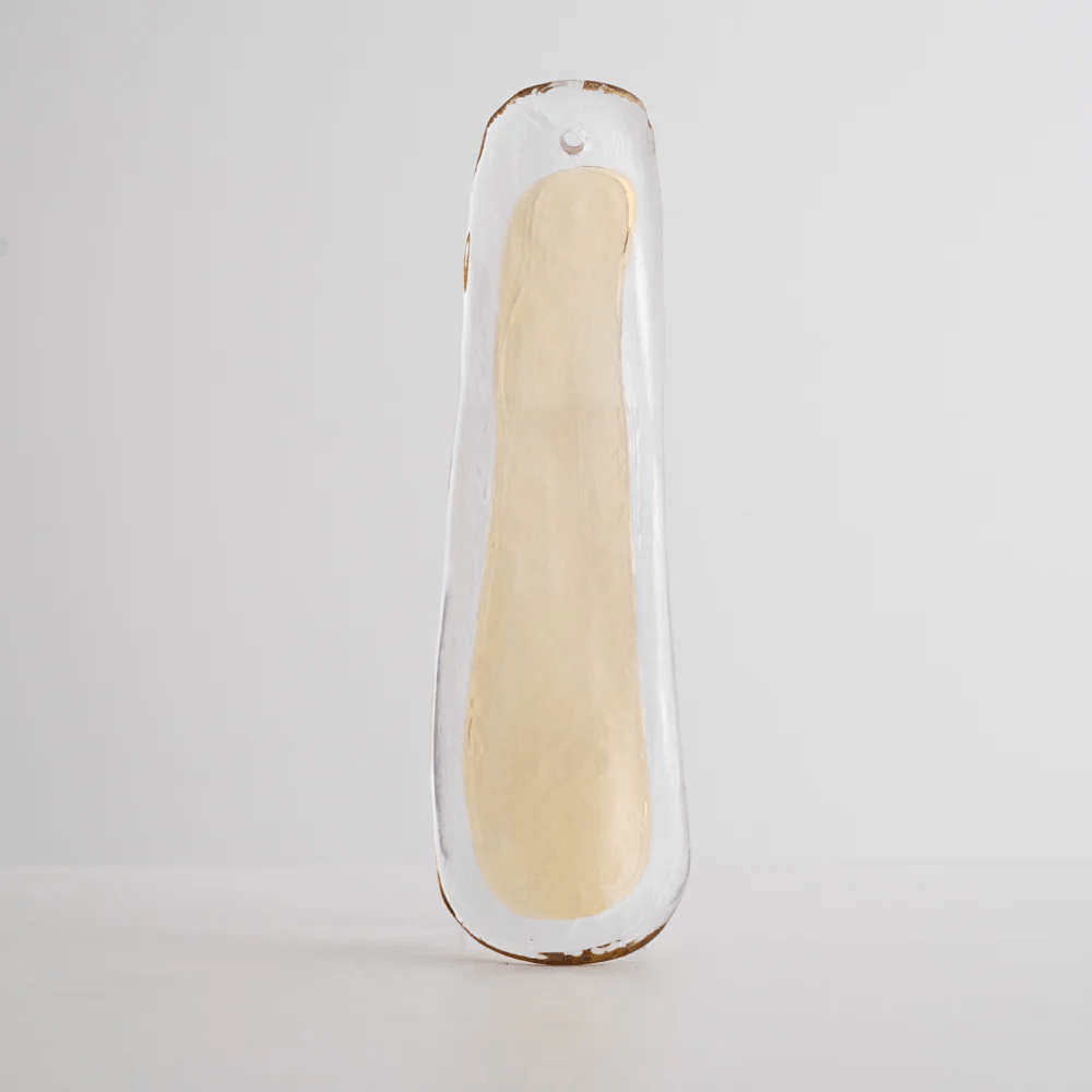 A clear glass leaf with a cream centre and a hanging hole at the top, photographed on grey for this Clérachic chandelier.