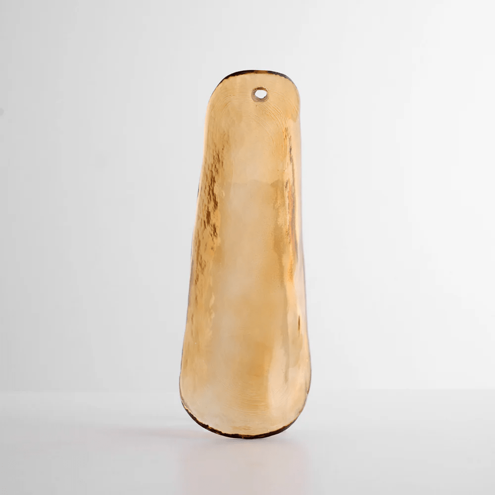 Close view of a single honey-amber glass leaf with a darker edge, upright on a soft grey background, from Clérachic.