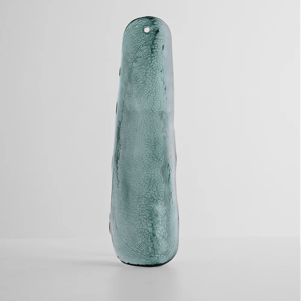 Single teal-blue glass leaf with a fine crackled texture, standing on a pale grey backdrop for this Clérachic chandelier.