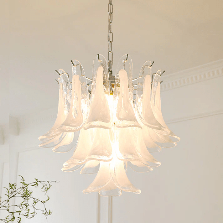 Close view of a frosted white glass leaf chandelier from Clérachic, lit warm in front of cornice moulding and a thin branch.
