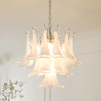 Close view of a frosted white glass leaf chandelier from Clérachic, lit warm in front of cornice moulding and a thin branch.