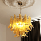 Bright amber glass leaves on a Clérachic chandelier, hung from a plaster ceiling rose in front of dark curtains.