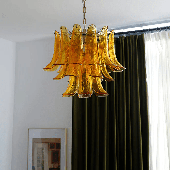 Golden amber glass leaf chandelier from Clérachic hanging in front of olive-green curtains, with a framed print below.
