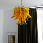 Golden amber glass leaf chandelier from Clérachic hanging in front of olive-green curtains, with a framed print below.